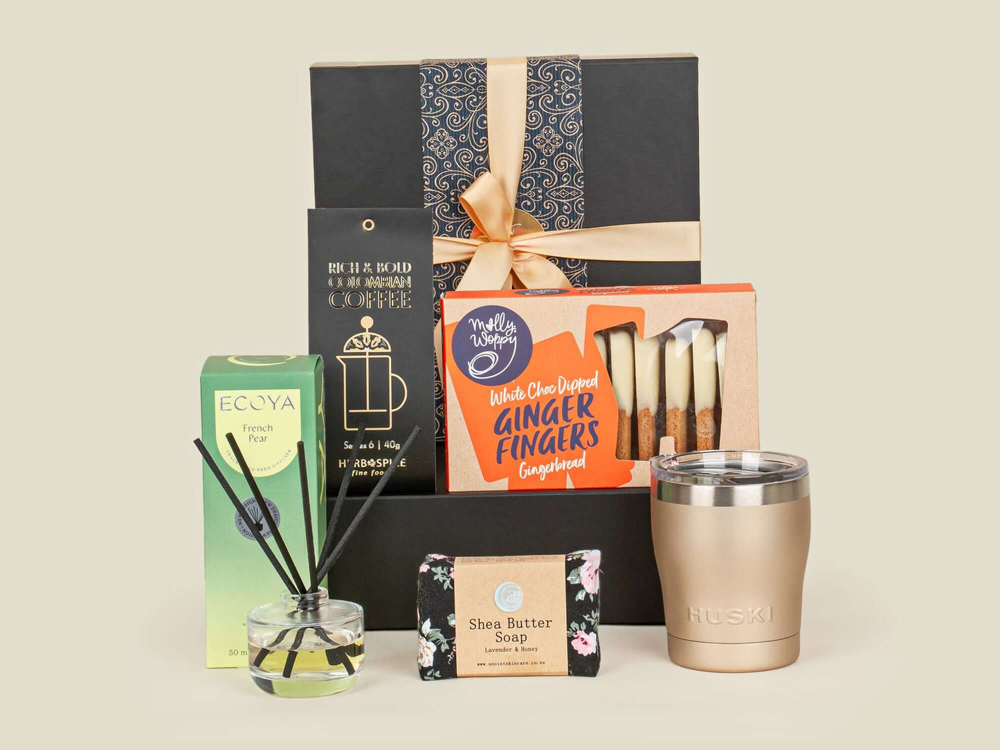 Collection of gift items including a mug, candles, soap, and a diffuser on a beige background
