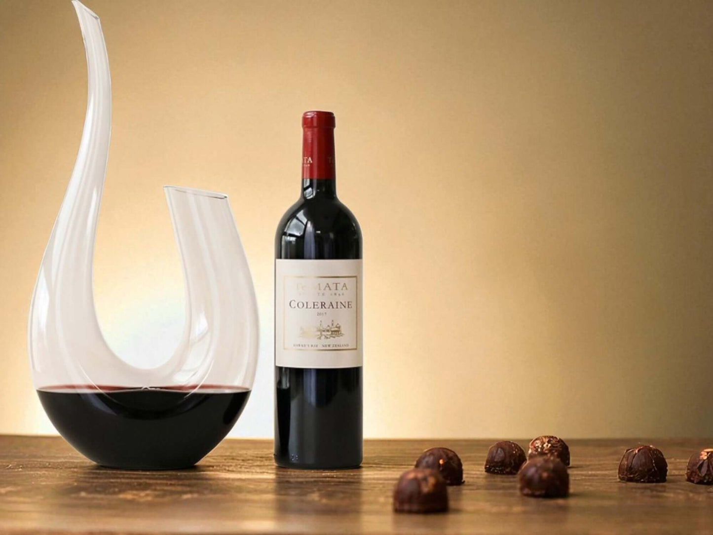 Bottle of Te Mata with a wine decanter and chocolates on a wooden surface.