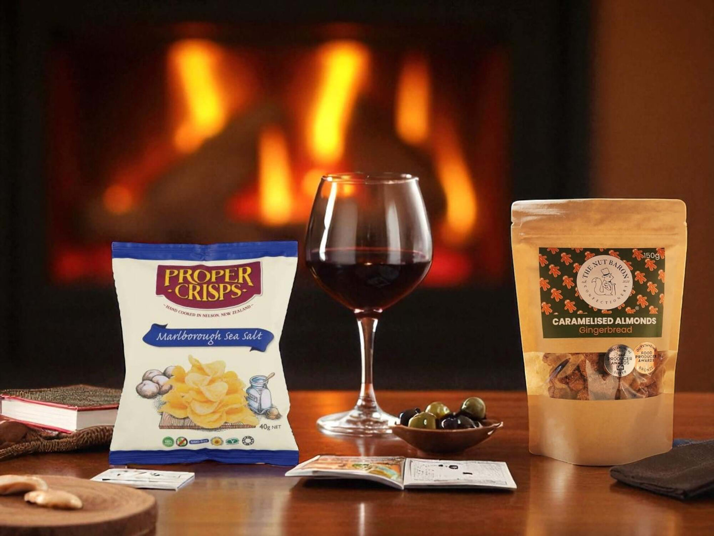 Table with snacks, a glass of red wine, and a book in front of a fireplace.