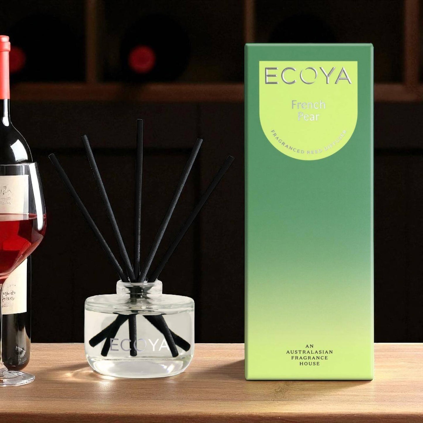 Ecoya diffuser and packaging on a wooden surface with a bottle of wine in the background.