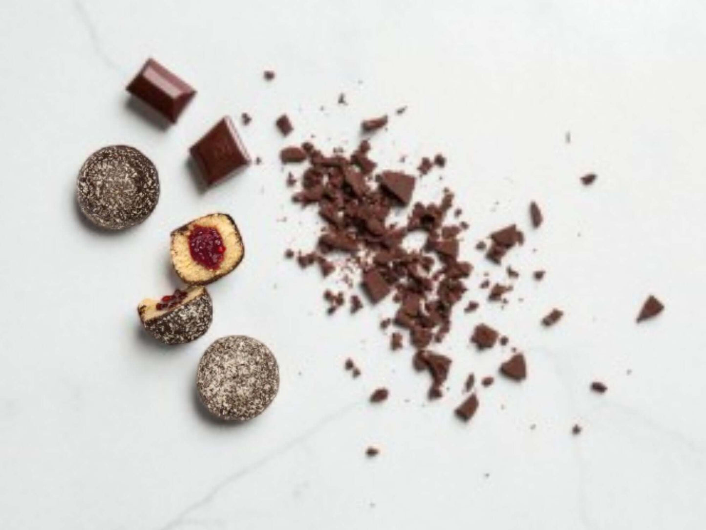 Chocolate truffles with a few pieces broken open on a white surface.