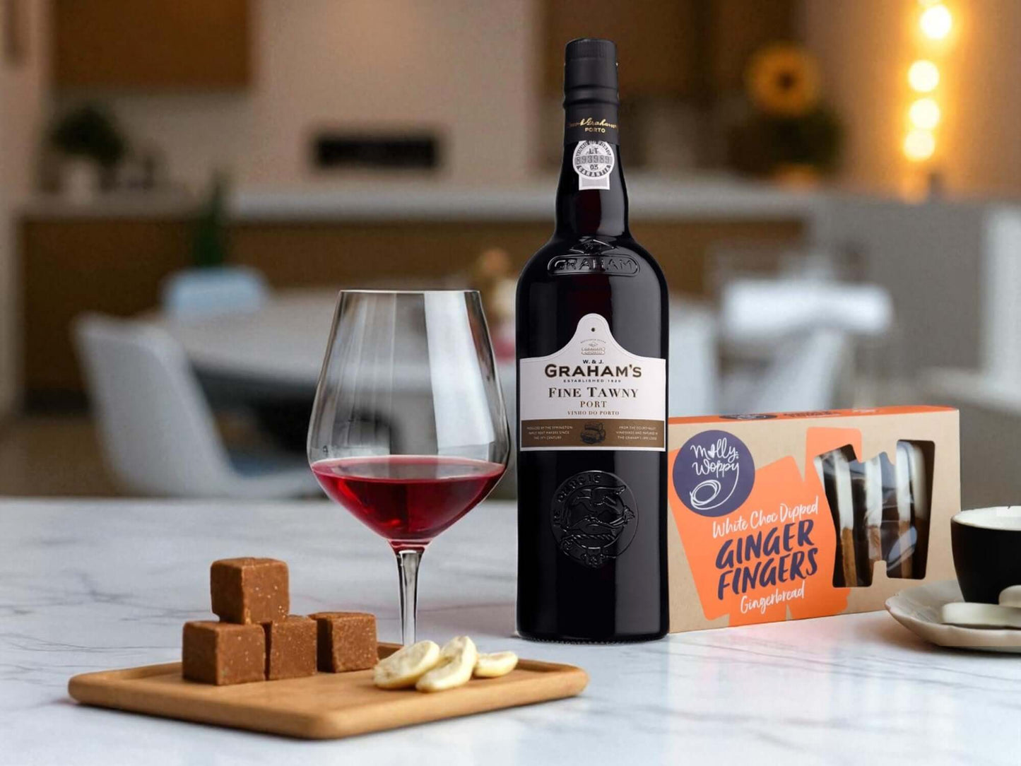 Bottle of Graham's Fine Tawny Port with a glass of red wine and ginger fingers on a table.
