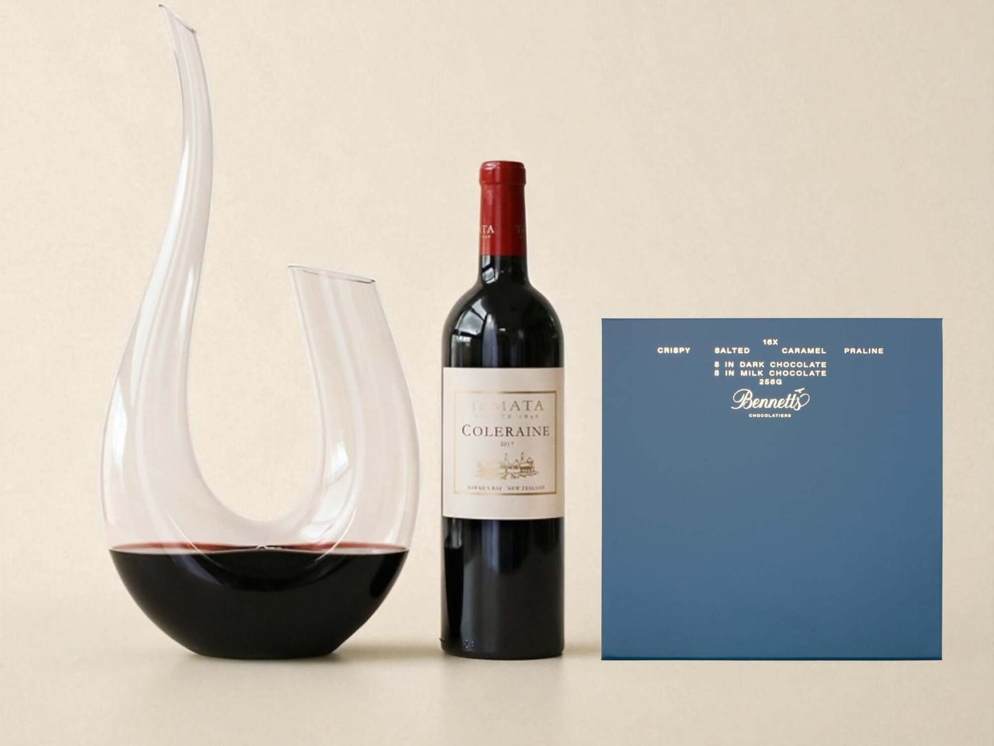 Wine decanter, bottle of red wine, and a blue box on a beige background