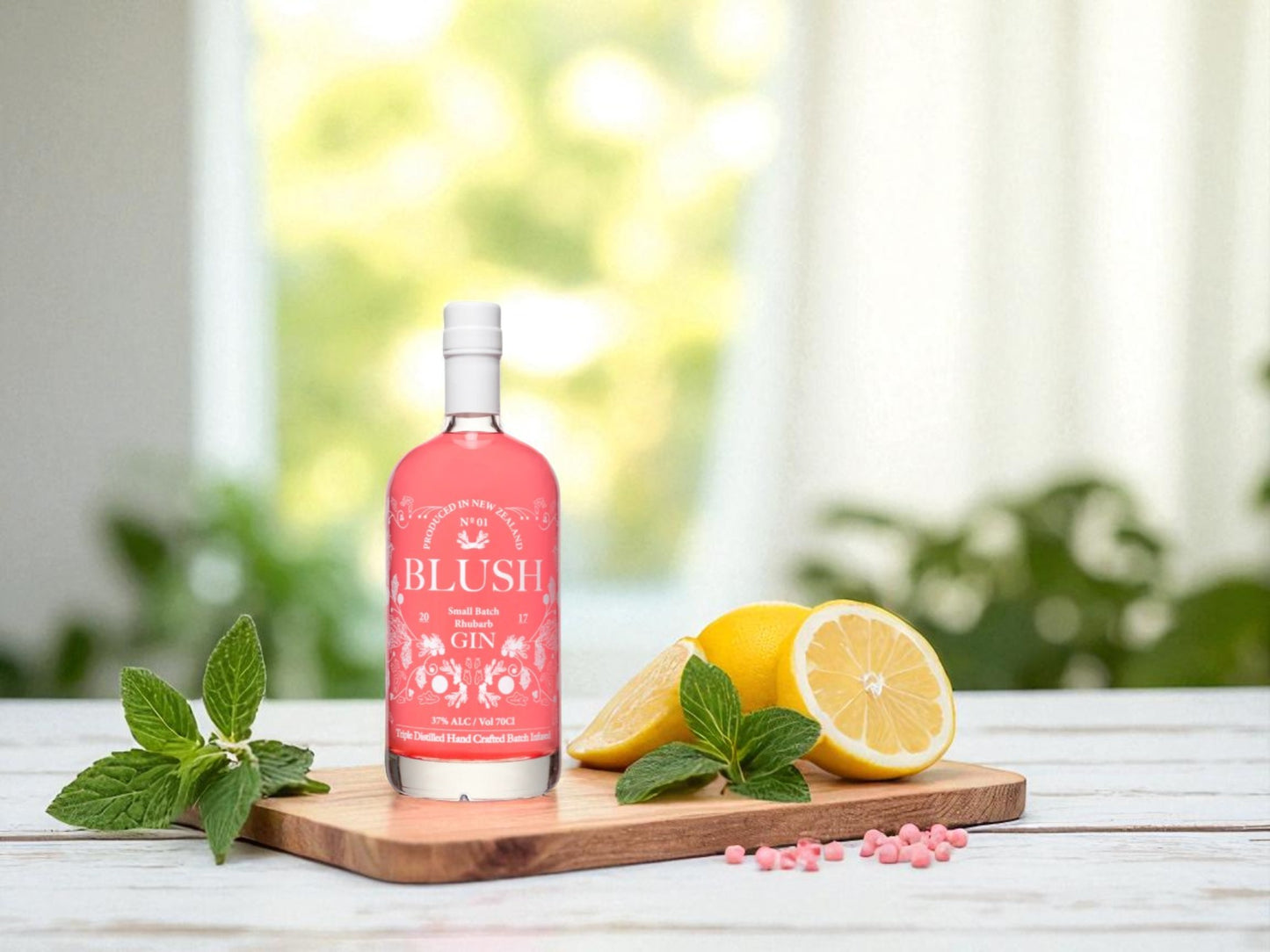 Pink bottle of Blush Gin on a wooden board with lemons and mint leaves outdoors.