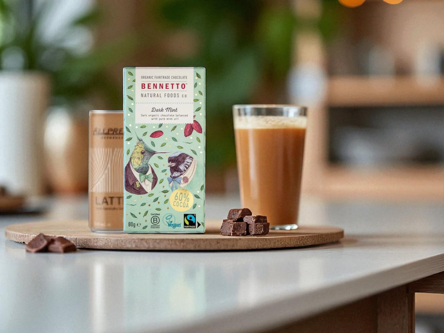 Bennetto chocolate bar packaging on a wooden board with a glass of coffee and chocolate pieces.