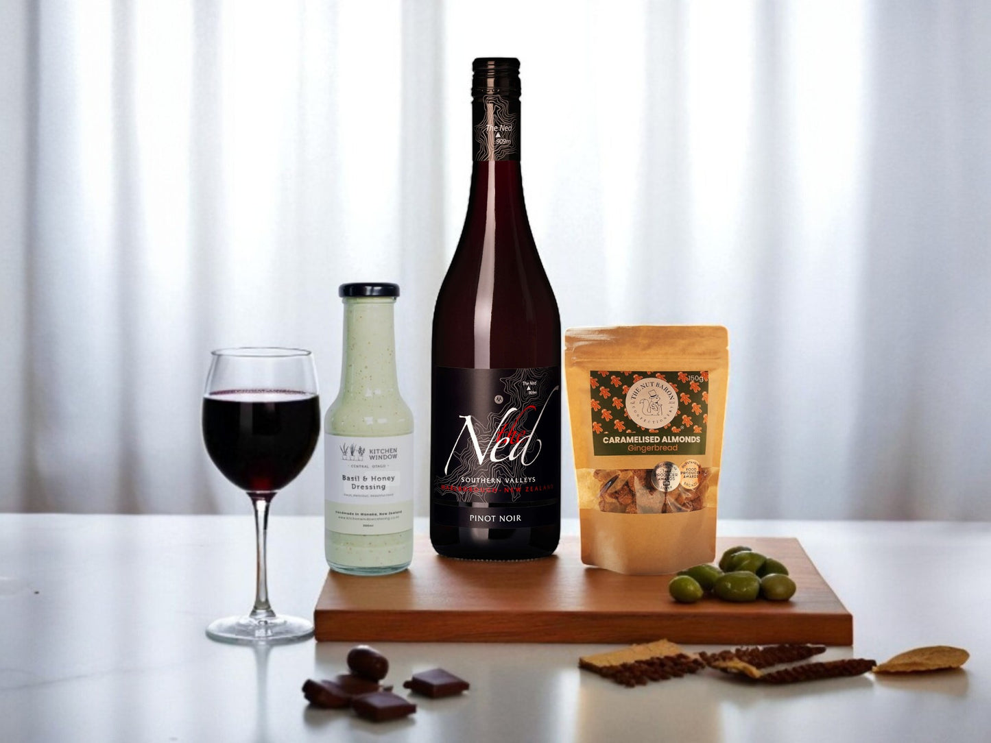 Wine bottle, glass of wine, and snacks on a table with a white curtain background