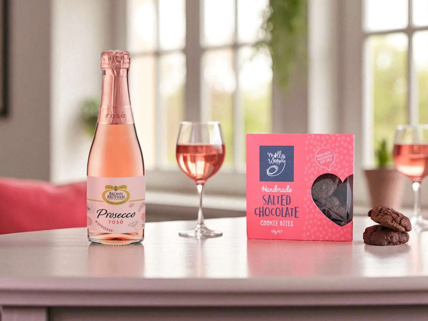 Bottle of Prosecco Rosé, glass of Prosecco, and box of chocolate cookies on a table.